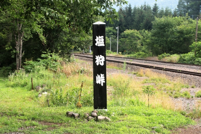 緑に囲まれた塩狩峠の標柱と、その横を走る鉄道の線路