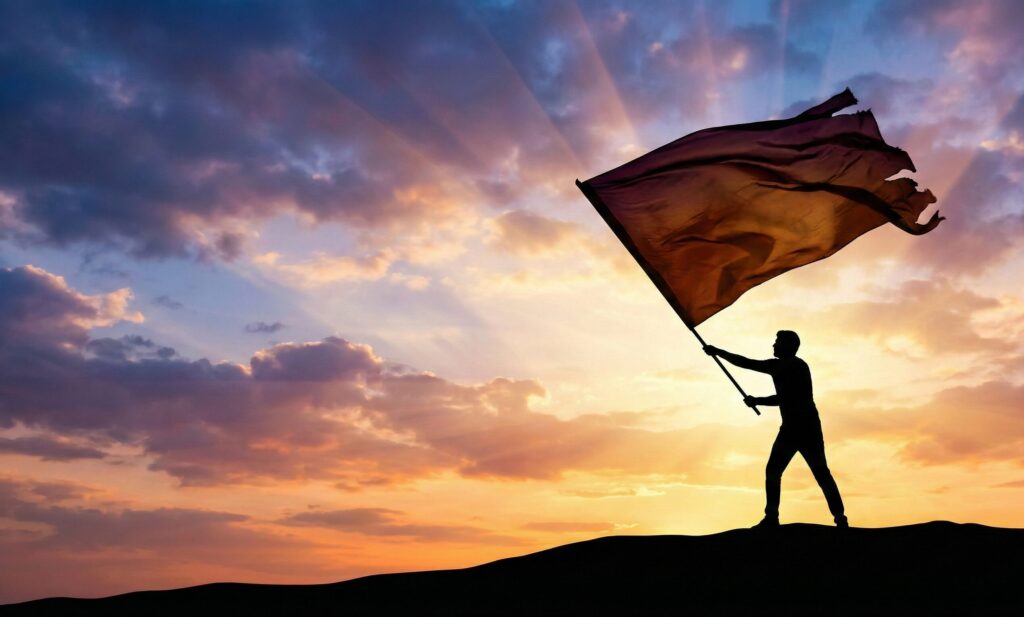 夕焼け空に向かって、丘の上で大きな旗を力強く振る人のシルエット